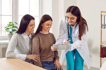 Smiling doctor holding report file with appointment and giving consultation to teeny girl patient...
