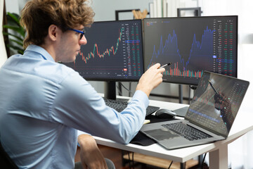 Young investor in stock trader pointing on dynamic exchange rate on laptop and pc screen in dynamic market graph online in real time at modern home office, analyzing financial technology data. Gusher. - obrazy, fototapety, plakaty