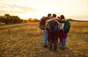 Team of huddling, hugging hikers. Group of happy smiling male and female friends with backpacks...
