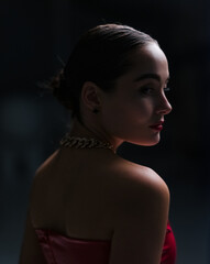 Portrait of litted young beautiful woman in dark studio with chain in her neck.