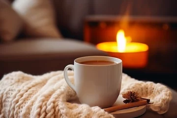 Foto op Plexiglas A mug of hot tea stands on a chair with a woolen blanket in a cozy living room with a fireplace. Cozy winter day © PhotoFlex