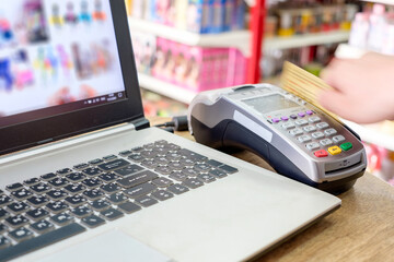 Hand swiping credit card on ternimal and using laptop payment shopping online
