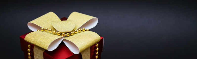 Red gift box with gold bow and beads on black background