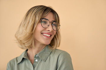 Smiling pretty gen z blonde young woman, happy college student girl with short blond hair wearing glasses looking aside standing isolated on beige background. Close up headshot portrait.