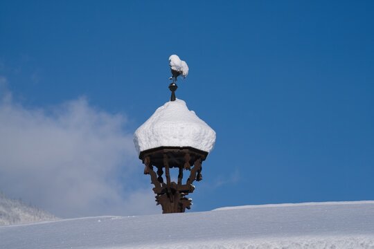 a snow covered antique weathercock on a roof at a sunny and cold winter day