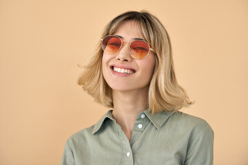 Happy pretty hipster gen z blonde young fashion woman, smiling cool cute girl with blond hair wearing trendy color sunglasses looking at camera isolated on beige background. Close up face portrait.