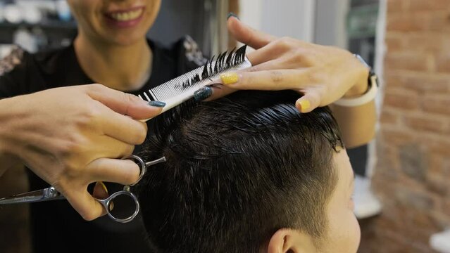 Reducing the length of black hair on the head of a woman with short hair. A smiling asian hairdresser works professionally with scissors and comb. The concept of providing quality services to clients