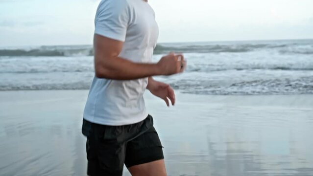 Man runs on the beach with sea in background in slow motion