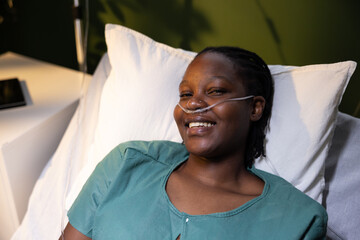 African woman lying in the hospital bed, wearing an oxygen tube, smiles at the camera.