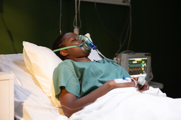 African woman in hospital, lying in bed, with oxygen mask closing eyes sleeping.