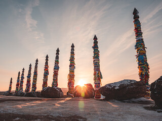 Traditional buryat shaman sacred pillars with colorful ribbons in winter at sunset, cape Burkhan,...