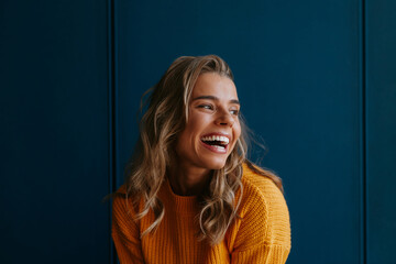 Happy young blond hair woman in yellow sweater looking away while standing on blue background