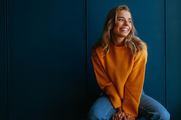 Happy young blond hair woman in yellow sweater looking away while sitting on blue background