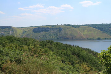 Fototapeta premium The Dniester River flows between mountains and hills covered with forests. A dense forest grows on the mountain near the river.