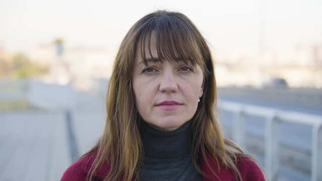 An attractive middle-aged Caucasian woman looks seriously at the camera by a busy road in an urban area - closeup