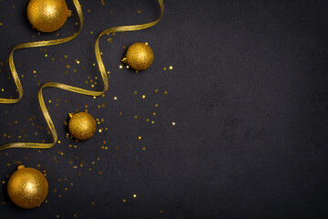 Golden Christmas ornament, ribbons and glittering star confetti on black background. Top view with...