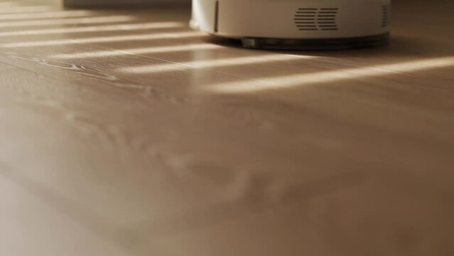 Automatic modern smart robotic vacuum cleaner cleans wooden floor. Smart home with automated devices that vacuums and washes laminate, simplify life. Housekeeping. Household Equipment. Sunlights.
