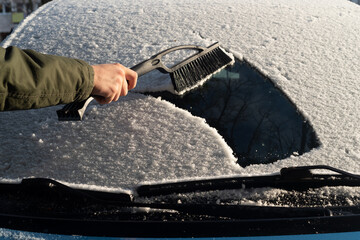 A young man cleans his car after a snowfall on a sunny, frosty day. Cleaning and clearing the car...