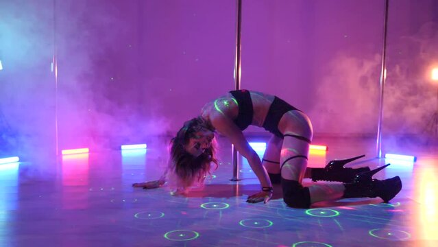 Sexy woman dances a pole dance in a disco club. Erotic dance on a pole. Exotic pole dance, stripper, pole sport, pole art. Smoke machine, laser.	