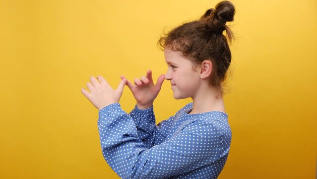 Kids humor concept. Profile portrait of funny caucasian little girl child teasing someone, playing with hands near nose, fooling around aside, posing isolated on yellow color background wall in studio