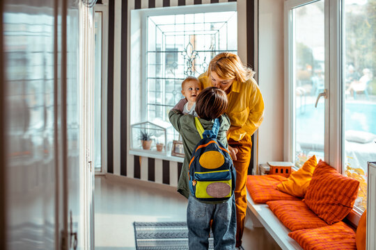 Boy going to school kissing goodbye mother and baby sister