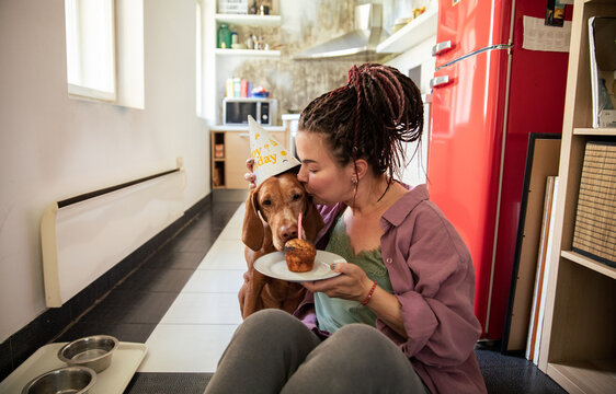 Woman celebrating dog birthday kissing pet at home