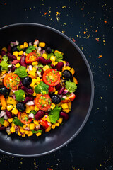 Mexican style salad - red beans, black olives, corn, yellow pepper, onion and tomatoes on wooden table