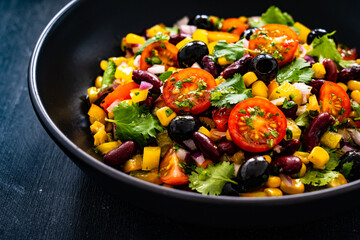 Mexican style salad - red beans, black olives, corn, yellow pepper, onion and tomatoes on wooden...