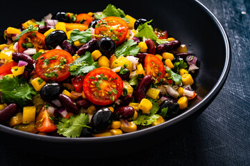 Mexican style salad - red beans, black olives, corn, yellow pepper, onion and tomatoes on wooden table