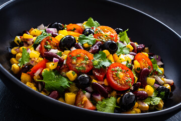 Mexican style salad - red beans, black olives, corn, yellow pepper, onion and tomatoes on wooden...