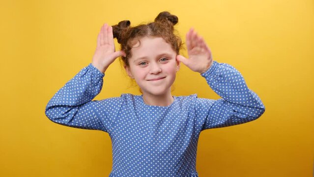 Misbehavior concept. Portrait of funny cute little girl kid sticking out tongue and grimacing looking at camera, holding hands near temples, posing isolated over yellow color background wall in studio