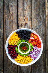 Mexican style salad - red beans, black olives, corn, yellow pepper, onion and tomatoes on wooden table