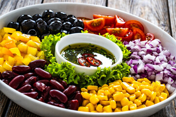 Mexican style salad - red beans, black olives, corn, yellow pepper, onion and tomatoes on wooden table