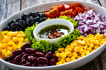 Mexican style salad - red beans, black olives, corn, yellow pepper, onion and tomatoes on wooden table