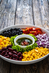 Mexican style salad - red beans, black olives, corn, yellow pepper, onion and tomatoes on wooden table
