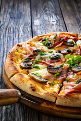 Pizza speck with ham, mozzarella cheese and white mushrooms on wooden table
