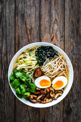 Asian style soup. Broth with chow mein noodles, boiled eggs, shiitake mushrooms, cilantro and mung sprouts on wooden table

