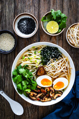 Asian style soup. Broth with chow mein noodles, boiled eggs, shiitake mushrooms, cilantro and mung sprouts on wooden table
