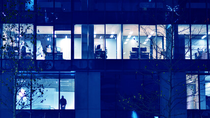 Fragment of the glass facade of a modern corporate building at night. Big glowing windows in modern...