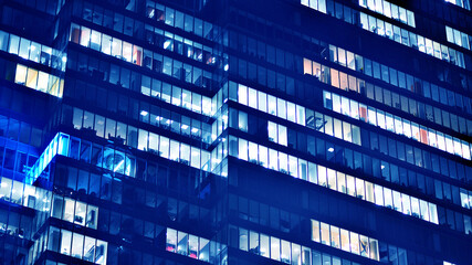 Fragment of the glass facade of a modern corporate building at night. Big glowing windows in modern...