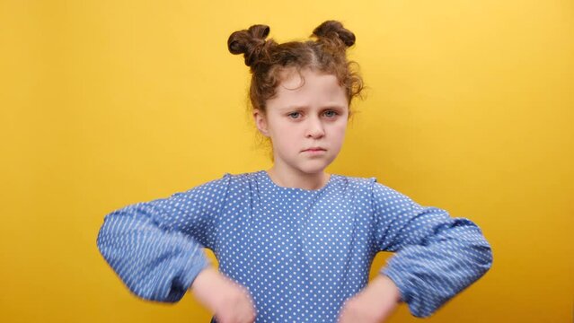 Portrait of little grumpy caucasian girl child pouting lips, grimacing and looking angrily to camera, posing isolated on plain yellow color background wall in studio. People emotion lifestyle concept