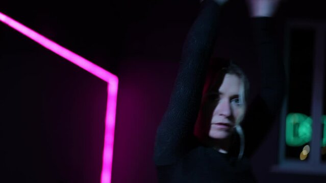 Live camera. Dancing woman in a choreographic hall with neon lighting. Close-up of the active waving of arms and gestures while performing the Waacking dance