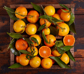 A wooden box with oranges and tangerines with leaves. Freshly picked up harvest of citrus fruits.