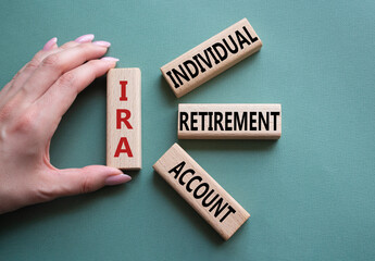 IRA - Individual Retirement Account symbol. Concept word IRA on wooden blocks. Businessman hand. Beautiful grey green background. Business and IRA concept. Copy space.