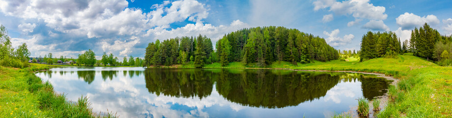 Fototapeta na wymiar Tranquil lake surrounded by green trees and meadow under cloudy sky.