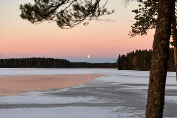 blue hour and moon rise on a lake in winter