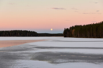 Sunset and moon rise on a lake in winter