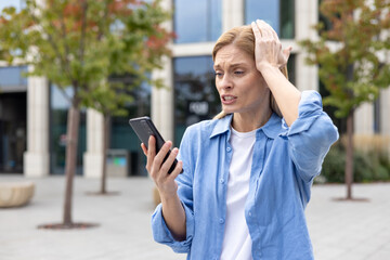 Mature woman outside office building in blue shirt sad received online message, female worker...