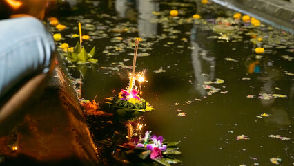 Photograph of 3 banana-leaf and orchid-flowering krathongs floating in a water source that is not...