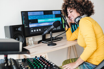 Female Latin host recording podcast on computer with headphones and microphone. Woman streaming...